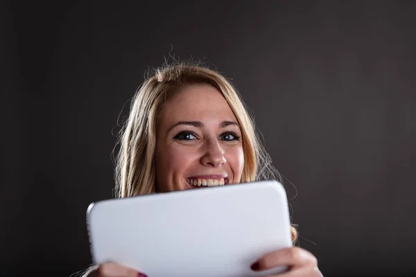 一个快乐的金发女人拿着一个数码平板电脑 她很高兴在网上发生的事情 比如一个新的系列季节 或者通过电子邮件的好消息 黑暗的对比背景 — 图库照片