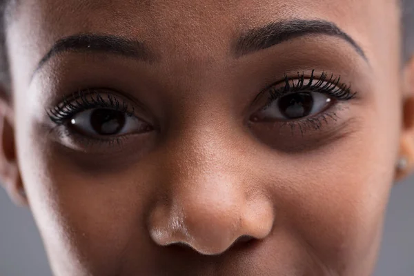 Close-up portrait of a young woman of color\'s eyes. Minimal depth of field, deer-like nose and eyes near. Mirror of the soul or checking for skin blemishes? Perfect eyebrows