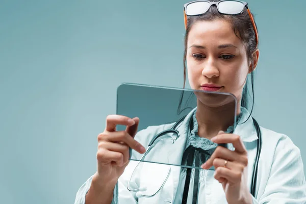若い女性医師は診断ツールとしてデジタルタブレットを使用し あなたのCopyspaceデータを研究しています グラフを自由に追加すると 未来的な透明な画面が空白になります 彼女はヘッドバンドとしてメガネを使用し Vです — ストック写真