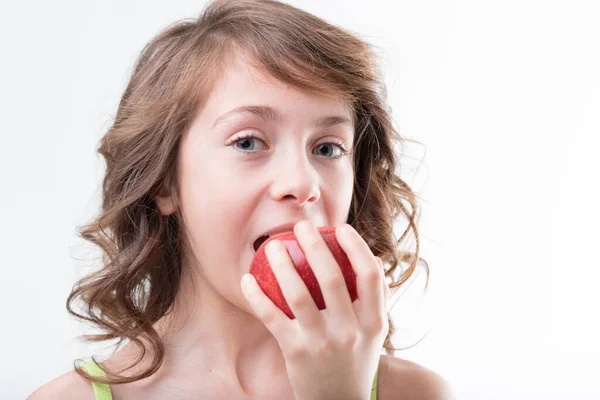 緑色のタンクの上のカーリー髪の少女は 健康的な習慣を象徴するジューシーな赤いリンゴに噛み付きます — ストック写真