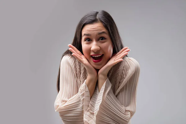 Frontal portrait of a joyfully surprised East Asian woman. Her hand gestures hint at whispered secrets - maybe shopping discounts, or romantic news? Captured on a neutral backdrop