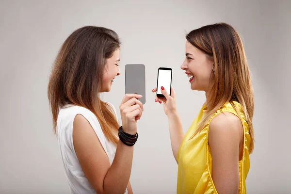Two young women share amusing, spicy gossip, make fun of others' behaviors, and use phones and social media to entertain each other