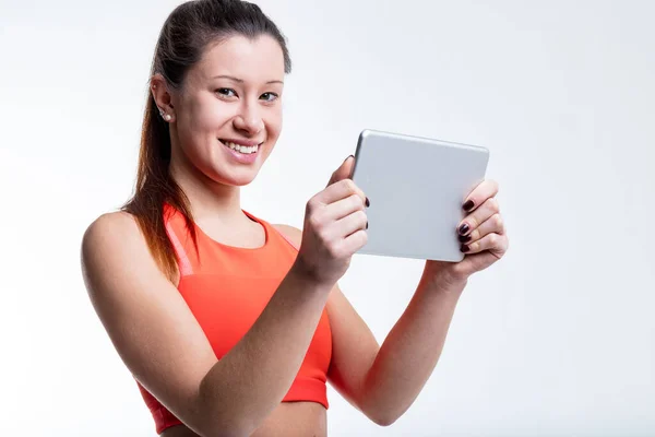 一位身披橙色运动上衣 身穿五颜六色的腿的东亚妇女 正在为自己的健身计划准备平板电脑 这证明了她的决心 — 图库照片