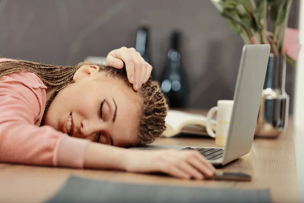 Exhausted from work or studying, a woman with box-braids falls asleep at her laptop, hand on phone