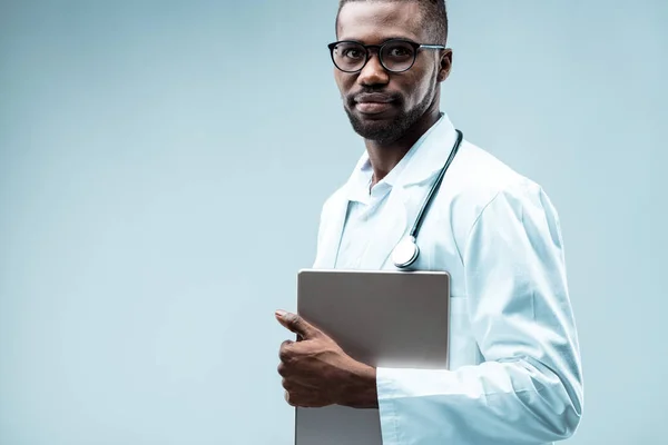 Black doctor with a tablet, benefits from digital tech. Wears white coat, stethoscope, multiple degrees, internships, and is also attractive