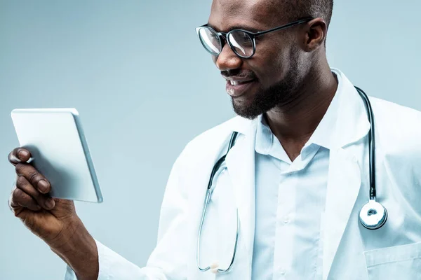 Modern physician with groomed beard, using high-tech tools for patient care. Black, holding a tablet, well-educated with degrees, attractive