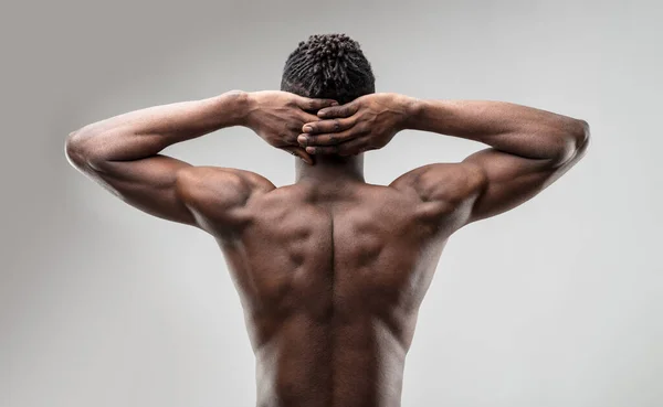 young, toned black man's bare back; arms up and clasped behind his head. His athletic form emphasizes his desirability and gym effort