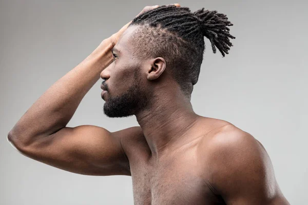 Profile of a black man with a well-groomed beard, bare chest and shoulders, aware of his beauty and toned physique. Posing vainly and charmingly