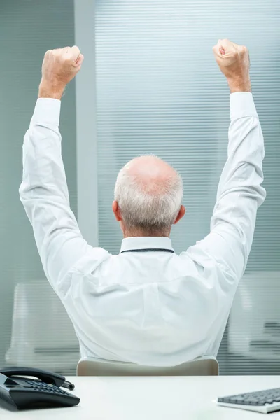 senior businessman, viewed from behind, raises his arms in sheer joy and triumph. The visible hairless center is framed by white hair, symbolic of age and wisdom in his white shirt and tie