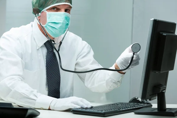 他是在修理病人还是在修理个人电脑 穿着医疗器械的人 带着听诊器 把它放在电脑上方 白衬衫和领带在前景中 办公室 医药或技术问题的结合体 — 图库照片