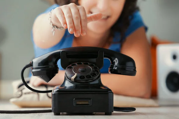 large vintage black dial phone foregrounds direct human communication. It stands as a testament to answering and conversing. In the background, a young woman, slightly out of focus, moves her hand to