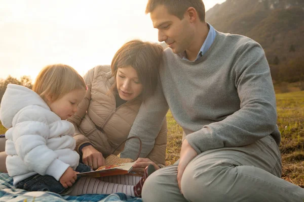 Amidst a picturesque outdoor setting, at the mountain\'s base, a young family bonds over an illustrated book. This unit symbolizes the very foundation of a Nation
