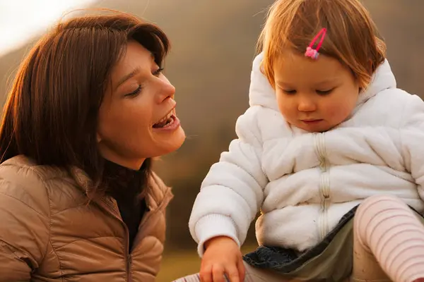 mother lovingly sings a biblical psalm to her daughter as they play outdoors during autumn at the foot of a mountain. They bask in the sunlight, cherishing family time as sacred, blessed by the Holy T