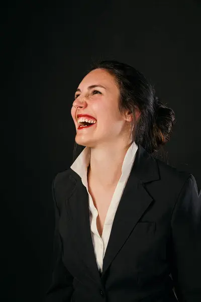 Laughing woman in black business outfit against a black background. Clear competence, value, and vivid beauty. Enjoying a joyful moment, shes ready to face life\'s challenges again, responsible for her success