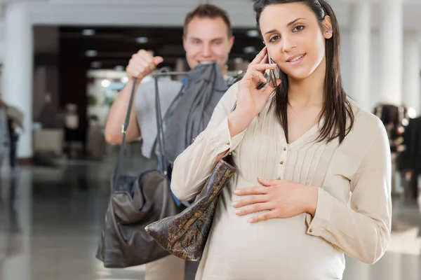 Husband carries bags, following his pregnant wife as she talks on the phone, oblivious. Highlighting the idea of maternity and a dysfunctional relationship