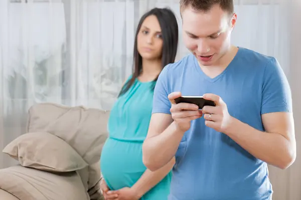 Беременная Молодая Женщина Наблюдает Мужчиной Погруженным Игры Телефоне Отражая Важную — стоковое фото