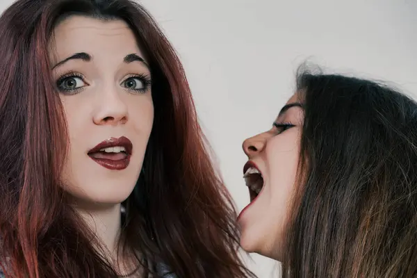 In a delightful mix of beauty and jest, two women with long, perfectly styled hair and makeup make quirky faces, laughing and enjoying their time
