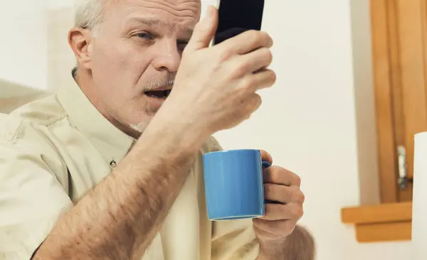 Breakfast time: An elderly man in the kitchen squints at his phone. Modern designs aren't for those with vision troubles. An eye doctor's visit and spectacles could be solutions