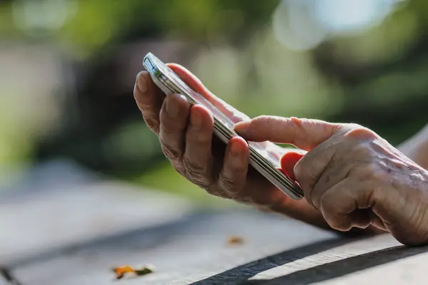 在崎岖的公园木头上 一个老年人的手指在和电话摔跤 今天的科技规模小 又敏感 将老年人推向社会隔离 — 图库照片
