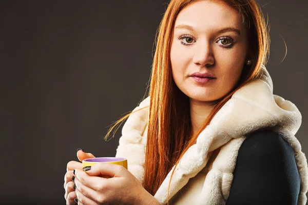 Woman finds comfort in a hot beverage, her attire suggesting a break from the chill outside