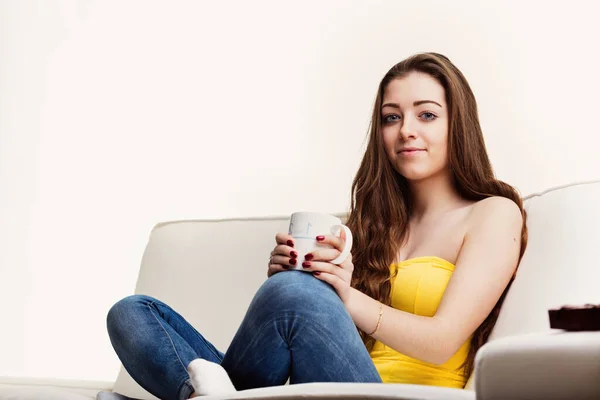 Young woman relaxes on a sofa, holding a mug with both hands