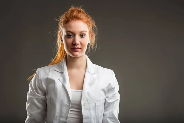 Technical specialist in a lab coat stands with determination, her red hair marking a bold presence in a field of precision