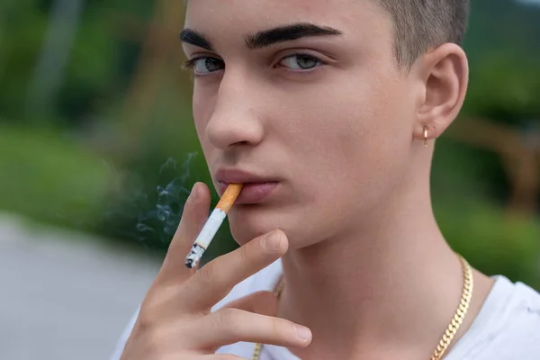 在一片朦胧的背景中 脸色苍白的年轻人喜欢抽烟 耳颈上点缀着珠宝 — 图库照片