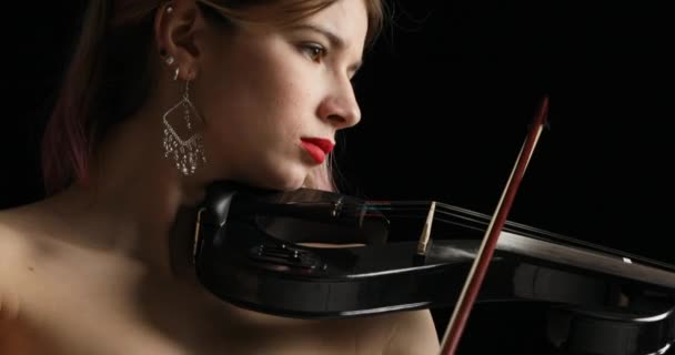 垂直カメラスイープは スコアに囲まれた暗い背景に設定された電気バイオリンを再生する黒の女性をキャプチャします — ストック動画