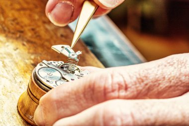Skilled hands bring life to metal, as the heart of a watch is finely tuned clipart