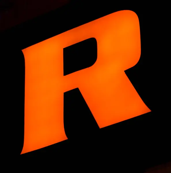 stock image Captured from below is a striking, luminous 'R' set against a dark backdrop. Its audacious orange hue stands out vividly, contrasting sharply with its surroundings. Such a design choice might signify 
