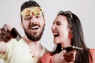 Couple laughs loudly, pointing their phones at the camera, their exuberance and loud demeanor drawing attention in a playful yet overwhelming way clipart