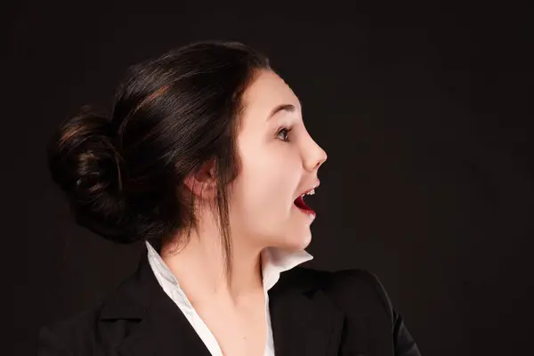 stock image Expressive young professional shows a spontaneous reaction of surprise, her facial expression vivid against the dark backdrop