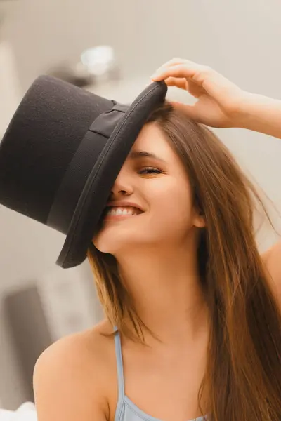 stock image Bright-eyed woman with long hair enjoys a playful moment with a black hat, her joy evident in her radiant smile
