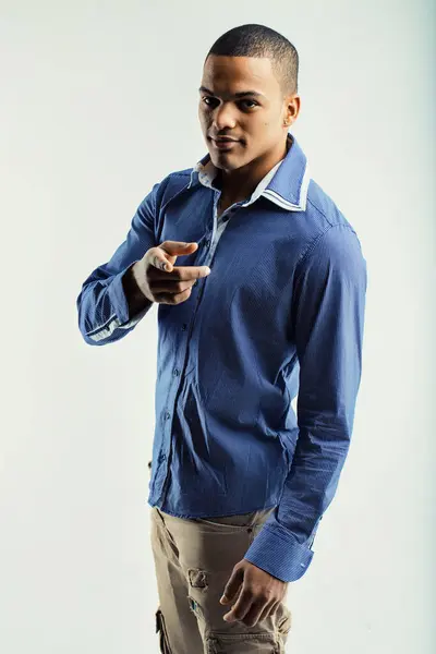 Stock image oung man in a blue striped shirt and beige pants, pointing forward with a confident expression. His casual attire and assertive gesture convey confidence and directness