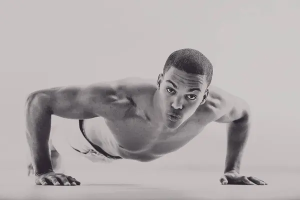 stock image Muscular black man in vintage 1950s style doing push-ups, showcasing his physical strength and determination. His intense gaze and defined muscles emphasize his commitment to boxing