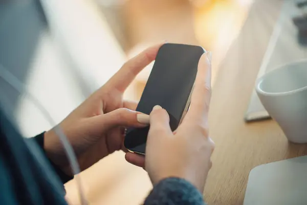 stock image Close-up of hands using a smartphone with a blank screen, seated at a wooden table. A white coffee cup adds to the relaxed ambiance, hinting at a moment of quiet reflection