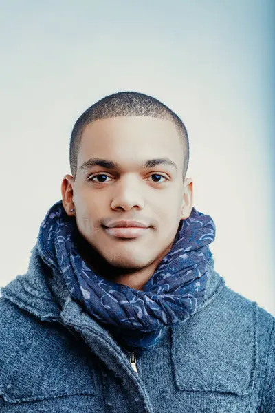 stock image Young man with a confident expression wearing a blue patterned scarf and a grey wool coat. His short hair is neatly trimmed, and he has a small earring in his left ear