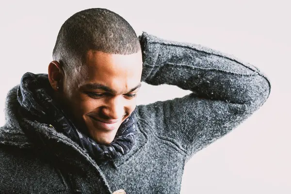 stock image Young man with a shy smile, looking down and touching the back of his head with his left hand. Dressed in a grey wool coat and blue scarf, his expression reveals embarrassment