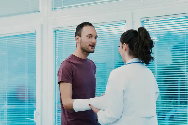 stock image Doctor is holding the arm of her patient who is describing how he got injured so she can decide on the proper treatment