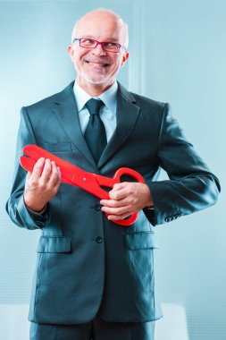 man in a suit holds large red scissors with a malicious smile, enjoying the power to make job cuts. His expression reveals a sadistic indifference to the hardship caused to families clipart