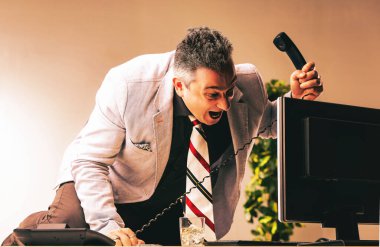 Businessman is yelling on his office phone while drinking alcohol at his desk, trying to appear courageous and strong despite feeling stressed issues of alcoholism in the workplace clipart