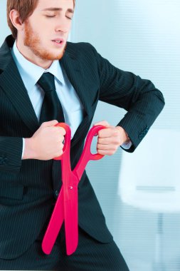 Businessman in a striped suit metaphorically cutting off his own profit by using oversized pink scissors, symbolizing self-defeating cuts clipart