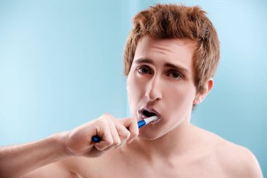 Young man with auburn hair brushes his teeth in the bathroom, showing his commitment to oral hygiene and self care clipart