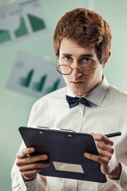 Young accountant is holding a clipboard and taking notes with a serious expression, suggesting focus and determination in his work clipart