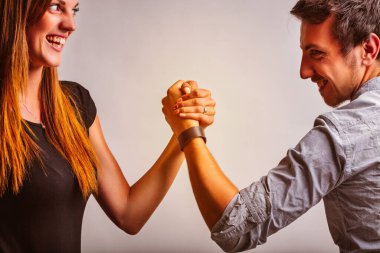 Smiling, a man and woman engage in a friendly arm-wrestling match, hands clasped tightly. Their determined expressions reflect mutual respect, support, and a symbolic balance of strength clipart