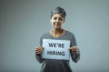 Confident businesswoman seeking new employees with a we're hiring sign, emphasizing determination and positivity in a professional setting clipart