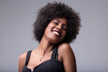 Young woman with curly afro hair and a radiant smile posing for a studio portrait, exuding happiness and confidence while looking directly at the camera clipart