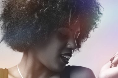 Black and white portrait featuring a young woman with an afro hairstyle, posing in a studio illuminated by colorful light effects, looking down and radiating a joyful smile clipart