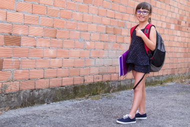 Sırt çantası ve kitapları olan mutlu öğrenci kız parmaklarıyla imza atıyor.