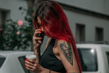 Kızıl saçlı kadın telefonda konuşuyor ve sokakta kahve içiyor.